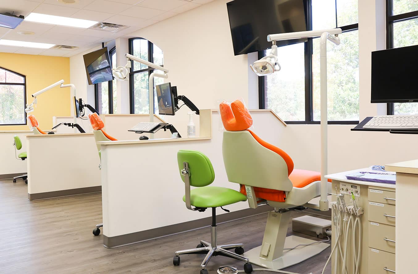 Modern pediatric dental office with colorful green and orange chairs, reception desk, and treatment area.