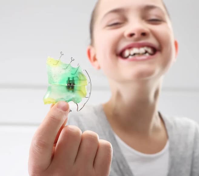 Smiling child holding colorful tooth-shaped object in bright dental office setting.
