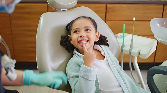 Young child in dental chair with finger in mouth during pediatric dental examination.