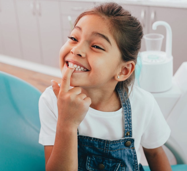 Young girl brushing teeth in bathroom with turquoise sink and mirror.