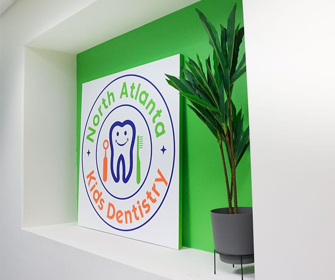 North Atlanta Kids Dentistry logo on green wall with potted plant in modern office setting.