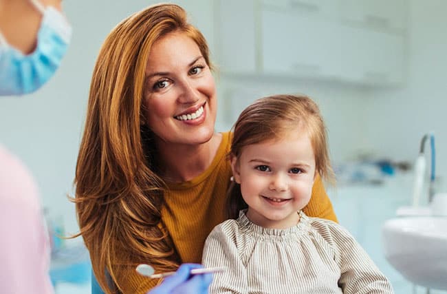 Smiling woman and young child in dental office exam room during checkup.