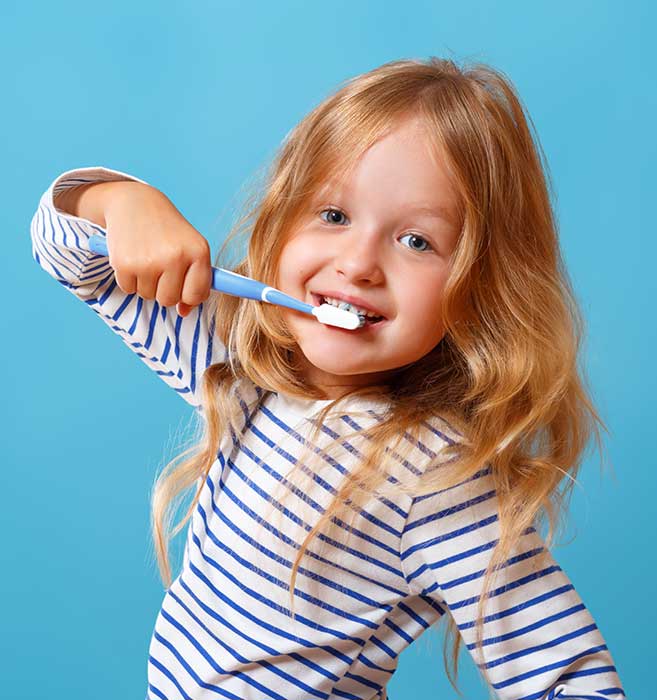 Smiling child with red hair brushing teeth against blue background, wearing striped shirt.