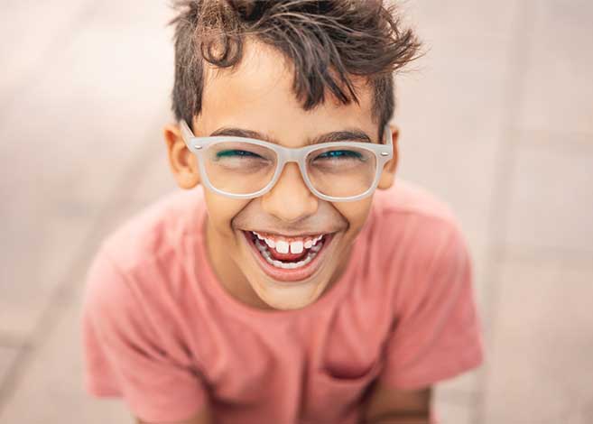 Happy child wearing glasses and pink shirt smiling at camera in dental office setting.