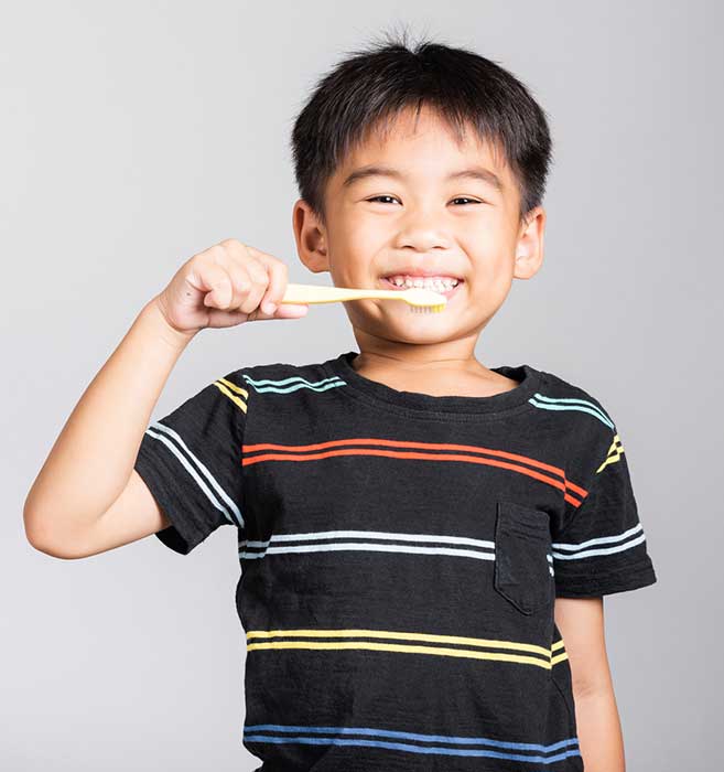 Young boy brushing teeth while smiling, wearing striped shirt against white background.